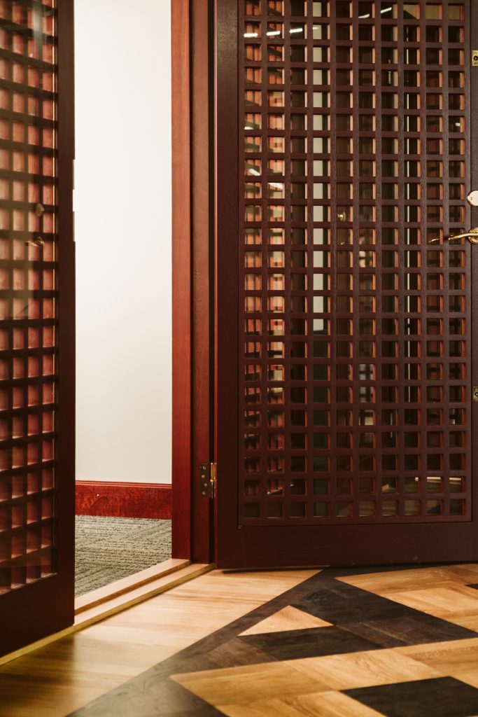 Trädörr med rutmönstrad panel i mörkt trä hos Banken, fotograferad tillsammans med golvdetaljer i ljus och mörk parkett.